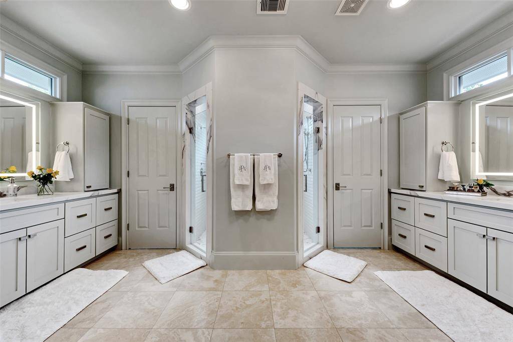 This spa-like primary bath features dual vanities with ample storage, two private water closets, and a central walk-in shower with and elegant tile. Soft lighting and natural tones create a serene, luxurious atmosphere for daily retreat.