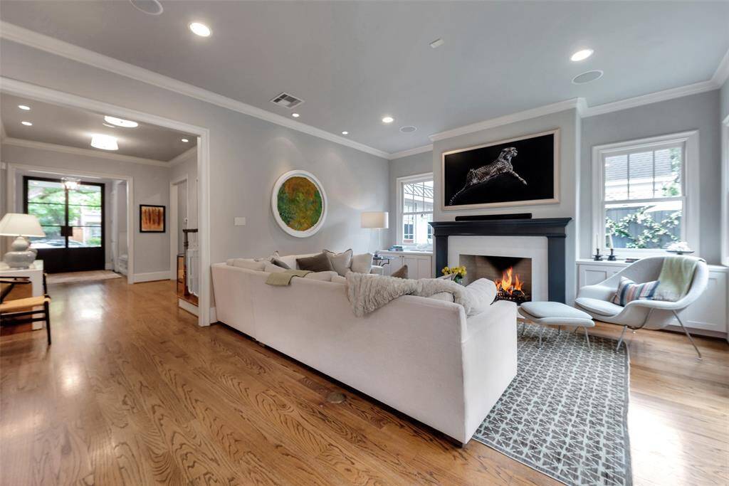 This inviting living room features an elegant fireplace framed by custom built-ins, wide-plank hardwood floors, and abundant natural light. The open layout flows seamlessly into the entry, creating a warm, modern space ideal for both relaxing and entertaining.
