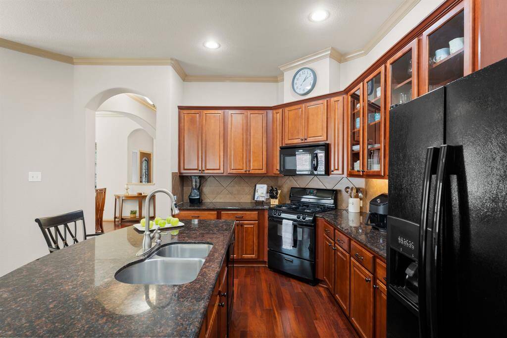 Chef’s kitchen with granite countertops, abundant cabinetry, gas range, and elegant glass-front display cabinets.