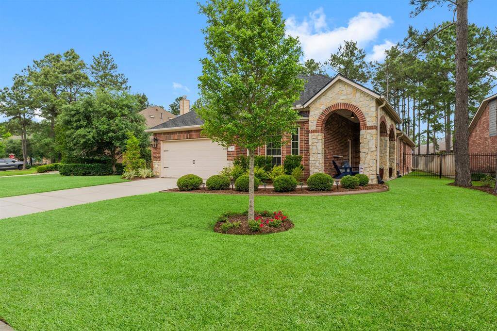 This wide-angle view highlights the serene setting beneath The Woodlands’ signature pine canopy, framing the home beautifully. The lush lawn and carefully sculpted beds offer an inviting sense of arrival.