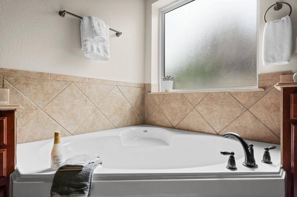 Unwind in the deep corner soaking tub, surrounded by neutral tile accents and softened natural light from the frosted privacy window—an ideal spot to recharge after a long day.