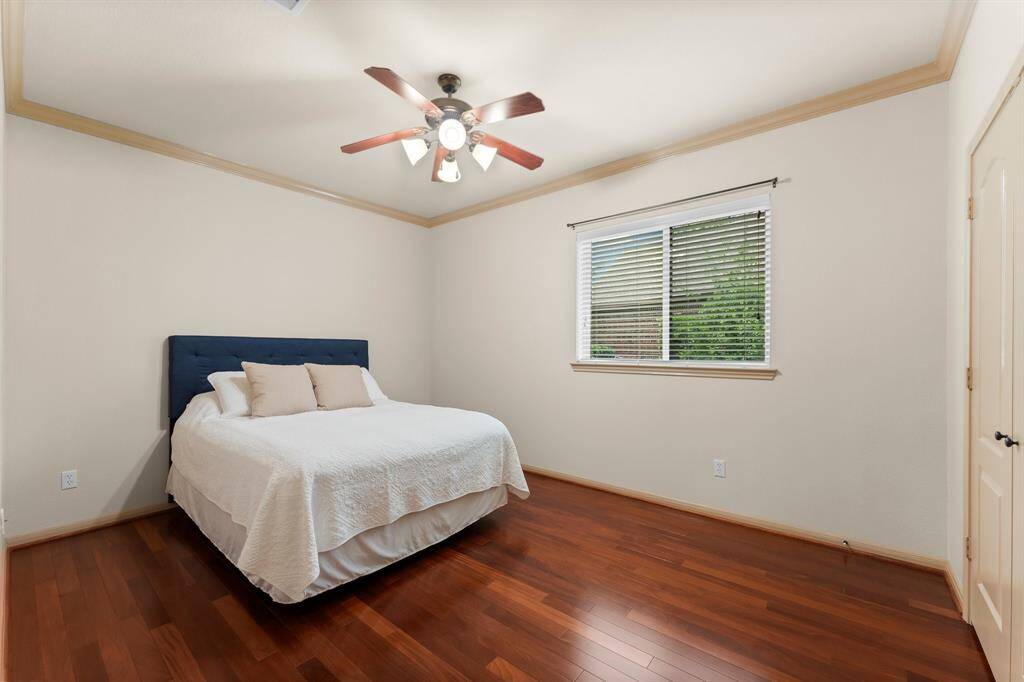 Secondary bedroom with hardwood floors, crown molding, big closet and a large window offering lush outdoor views.