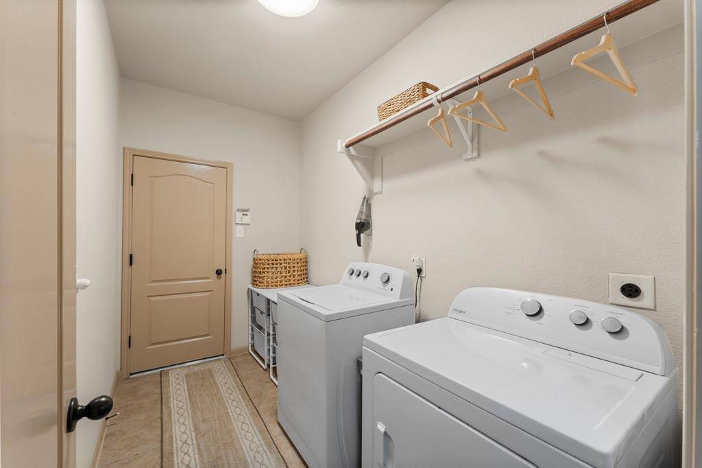 A generous utility room with built-in shelving and hanging space keeps household tasks organized. Tile flooring and direct access to the garage enhance both convenience and practicality.