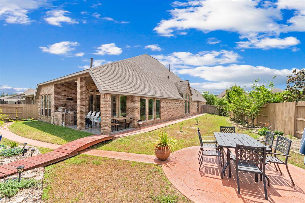The beautifully landscaped backyard features a large covered patio with an outdoor kitchen, perfect for entertaining or relaxing. A charming pergola adds a touch of elegance, creating a serene outdoor retreat.