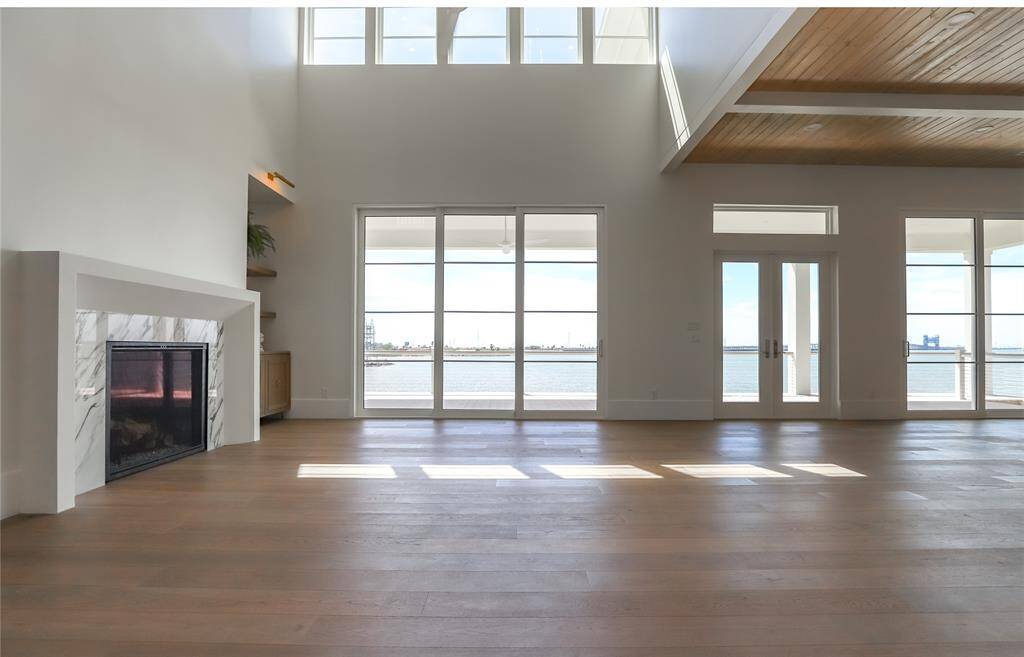Experience modern elegance in this spacious living area, featuring large glass doors and windows with breathtaking waterfront views. Enjoy abundant light, refreshing breezes, high ceilings, a sleek fireplace, and elegant wooden flooring.