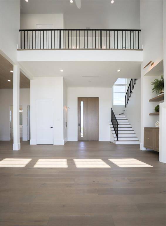 This spacious entryway features 10x5ft pivot front door, high ceilings, abundant natural light, and a modern staircase. The open layout highlights sleek finishes and a warm wood floor, creating an inviting atmosphere ideal for contemporary living.