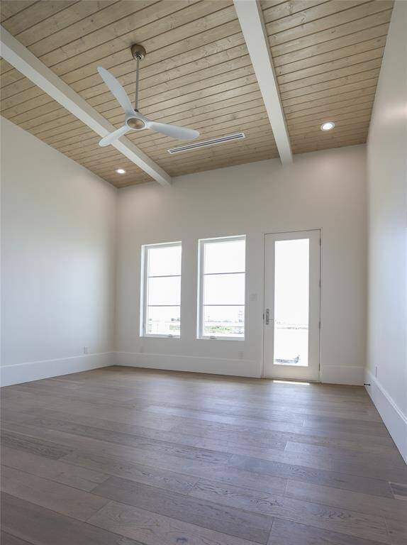 Bright primary bedroom on first level with high ceilings, featuring a modern ceiling fan and recessed lighting. It has three large windows and a glass door with entrance to porch, allowing plenty of natural light. The wood flooring and ceiling add warmth and character.