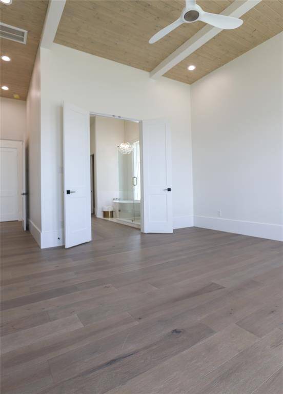 This spacious  first level primary bedroom features light wood flooring, high ceilings with recessed lighting, and a ceiling fan. It opens to a bathroom with double doors, creating a seamless flow between spaces.