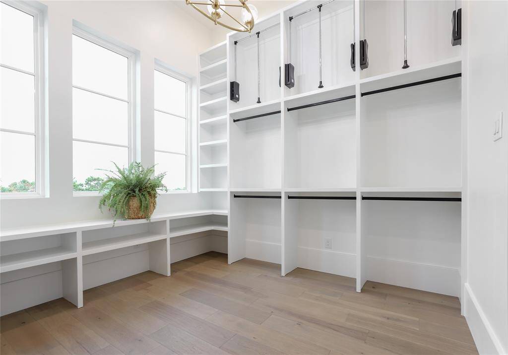 Spacious first level primary bedroom walk-in closet with ample shelving and hanging space, featuring three large windows for natural light and a stylish light fixture. Perfect for organizing and displaying clothing and accessories.