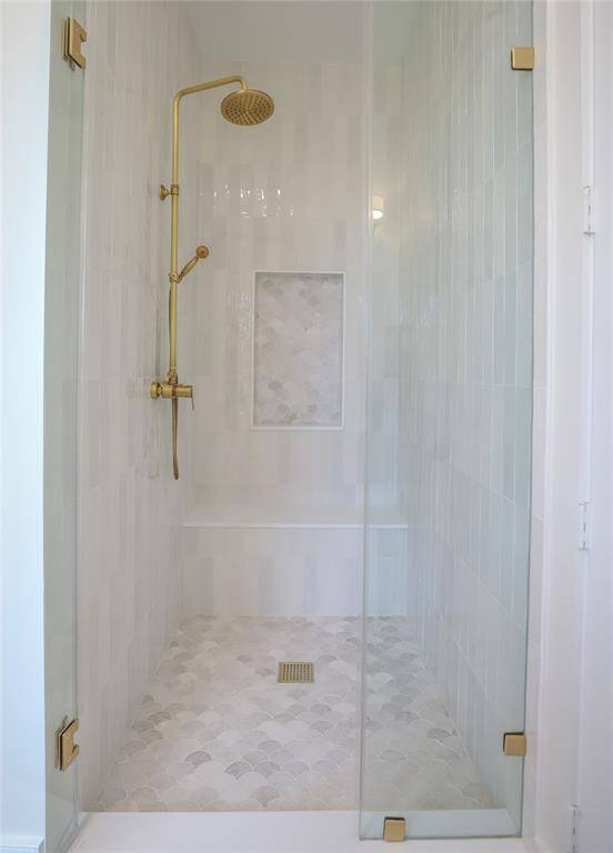 This photo shows a modern shower with elegant glass doors, a gold shower fixture, and light tiled walls and floor. There's a built-in niche for storage, adding functionality and style. Located on second floor in the jack and jill bathroom with access to 2 bedrooms.