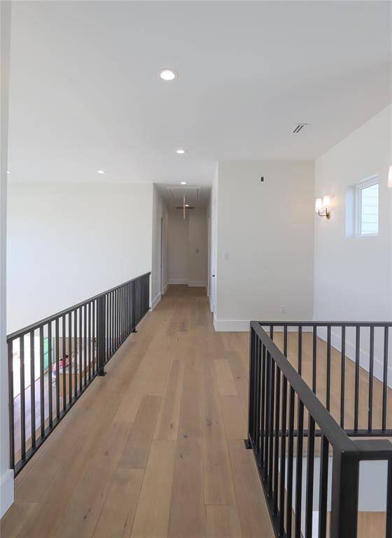 Bright and spacious hallway with modern wood flooring and sleek black railings, leading to multiple rooms. Ample natural light and recessed ceiling lights create a welcoming atmosphere.  Great area to add seating area.