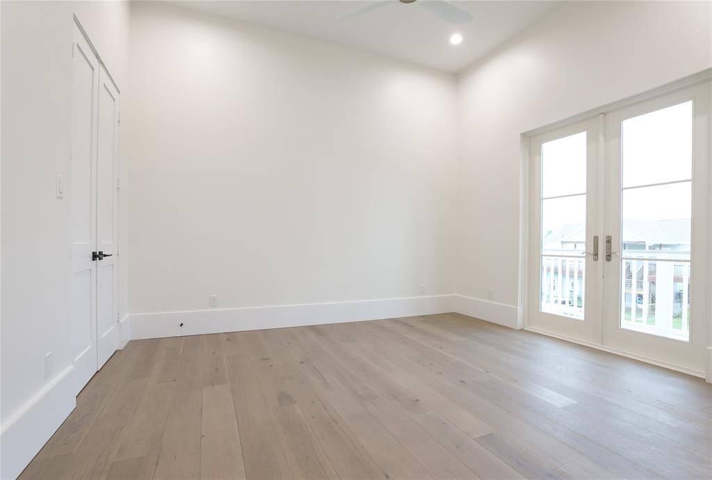 Bright, spacious bedroom on first level with high ceilings, light hardwood floors, and double doors leading to a balcony/porch.