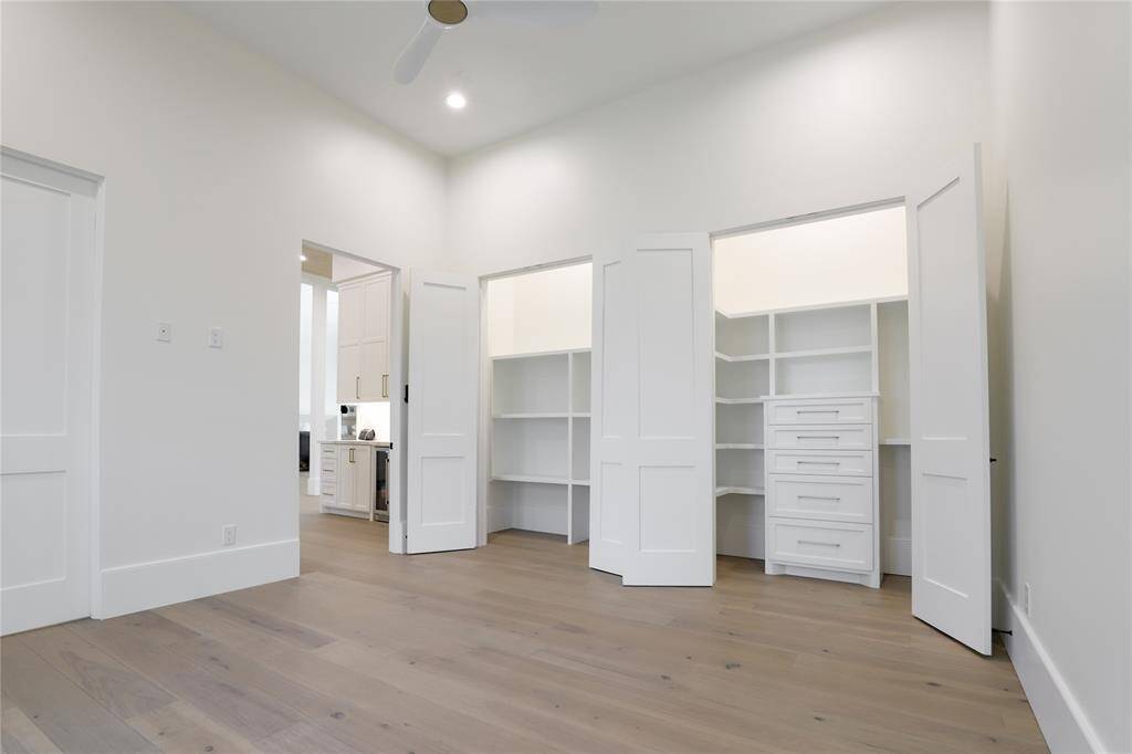 This first level bedroom features light wood flooring and ample natural light. It includes built-in closet with open shelves and drawers.