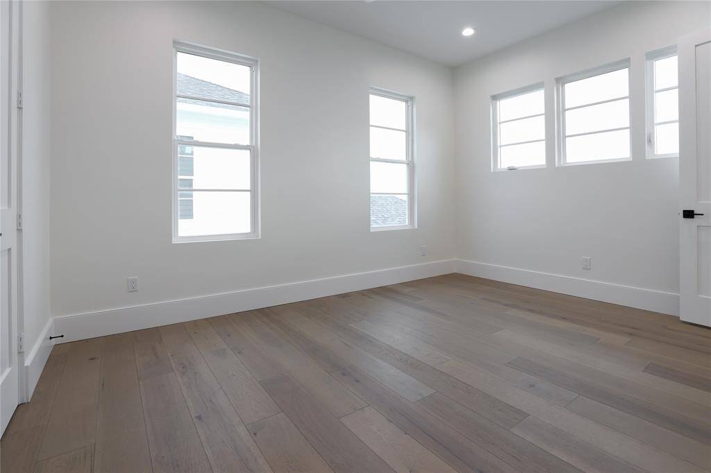 This second level bedroom features ample natural light with multiple windows and a modern, clean aesthetic. It has light wood flooring and neutral walls, creating a bright and airy space ideal for a bedroom or office.