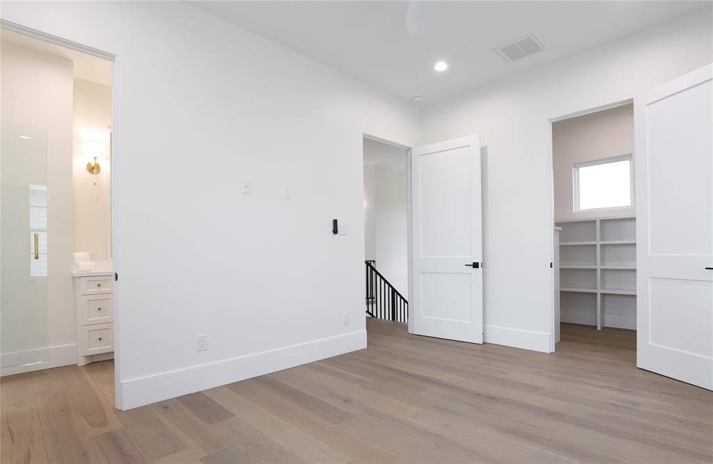 Bright, modern second floor bedroom with light wood flooring. Features a walk-in closet, en suite bathroom, and ample natural light through a small window. Clean, white walls enhance the spacious feel.