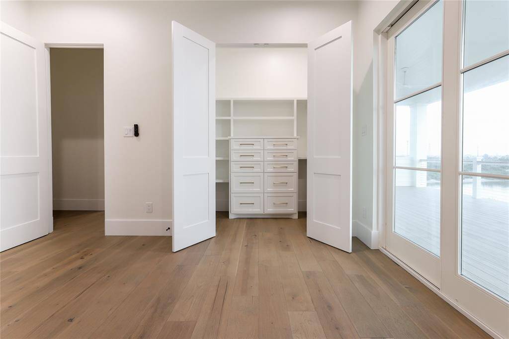 This second level bedroom features light wood flooring, a built-in closet with ample shelving and drawers, and large glass doors leading to a balcony, offering plenty of natural light.