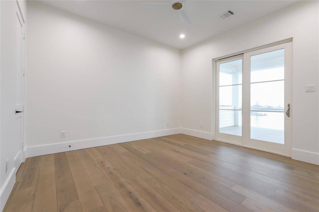 Bright second level bedroom with hardwood floors, featuring a ceiling fan and recessed lighting. French doors lead to a balcony with water views, creating a spacious and airy feel.