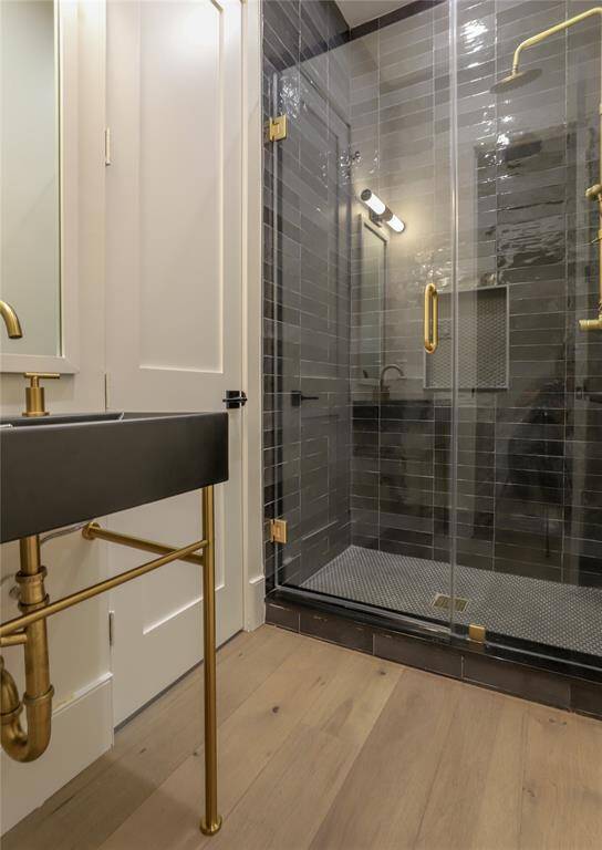 This modern bathroom features a sleek glass-enclosed shower with dark tiles and gold fixtures. The minimalist sink has a black basin and gold plumbing, set against light wood flooring, creating a stylish and contemporary look.