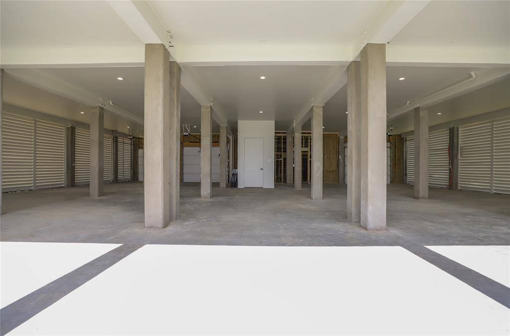 This photo shows a spacious and open garage area with multiple concrete columns, providing ample storage or parking space. The area is well-lit with a clean, modern finish, and features large shutter-style doors for easy access.