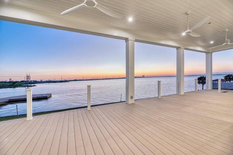 Spacious waterfront deck with panoramic sunset views, featuring a covered ceiling with fans, perfect for outdoor relaxation and entertaining.
