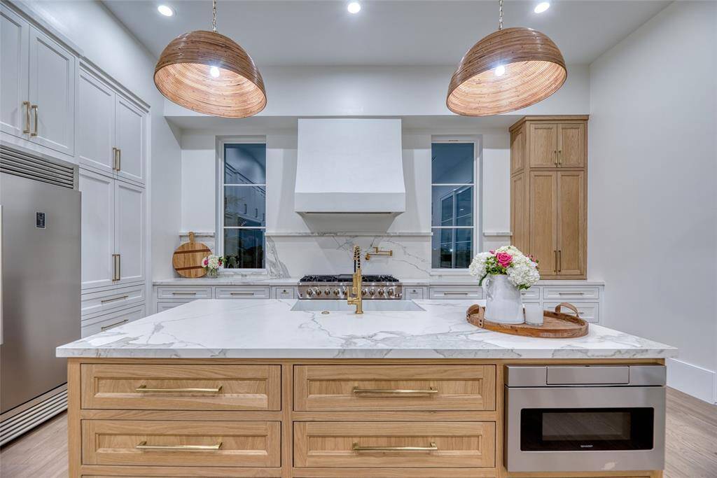 This modern kitchen features a spacious Neolith countertop island with elegant wooden drawers, stainless steel appliances, and stylish pendant lighting. The sleek design includes ample storage and a sophisticated range hood, perfect for culinary enthusiasts.
