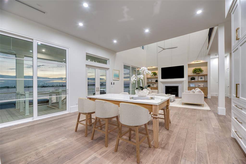 This modern, open-concept living space features high ceilings, a cozy fireplace, and large windows offering stunning water views. The dining area transitions smoothly into a comfortable lounge, highlighted by sleek finishes and abundant natural light. Wall to wall waterfront views.