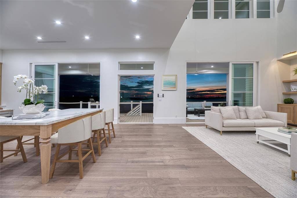 Experience modern living in this spacious open-plan area with hardwood floors, a chic dining space, and cozy seating. Revel in stunning sunset views through large windows, enhancing the bright, airy feel. Enjoy easy access to outdoor living with sliding and regular doors.