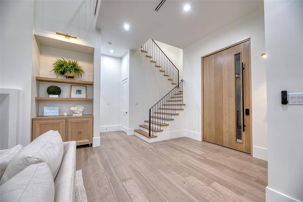 This photo showcases a modern, inviting entryway with a wooden 10x5ft pivot door for grand entry, sleek staircase, and built-in shelving. The space features light wood flooring, recessed lighting, and minimalist decor, creating a warm and contemporary atmosphere.