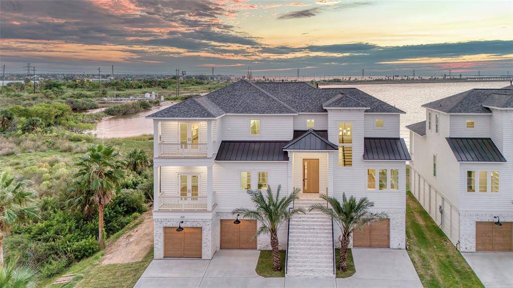 This stunning waterfront home features a modern three-story design with a clean white hardi plank exterior and brick accents. It offers an expansive view of the water, enhanced by large windows and a spacious entrance. The property includes a double garage and is surrounded by lush greenery, providing a serene and picturesque setting. Home next door is also for sale.