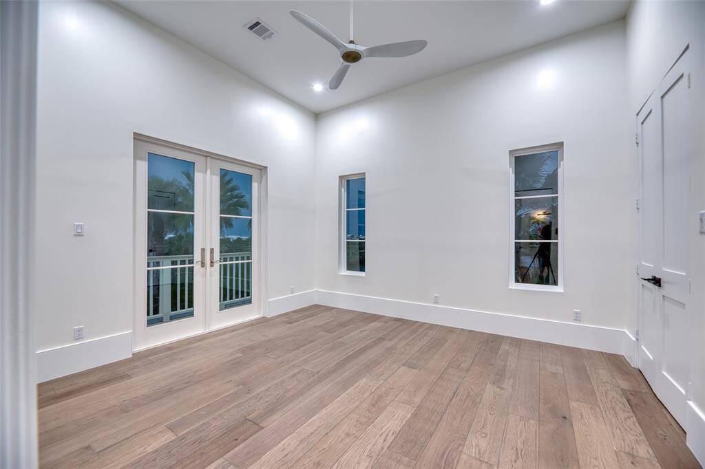 This  first level bedroom features sleek hardwood floors, a high ceiling with a modern fan, and ample natural light from French doors and tall windows. Perfect for creating a bright and airy living space or office. Outdoor balcony has beautiful water views for bird watching.