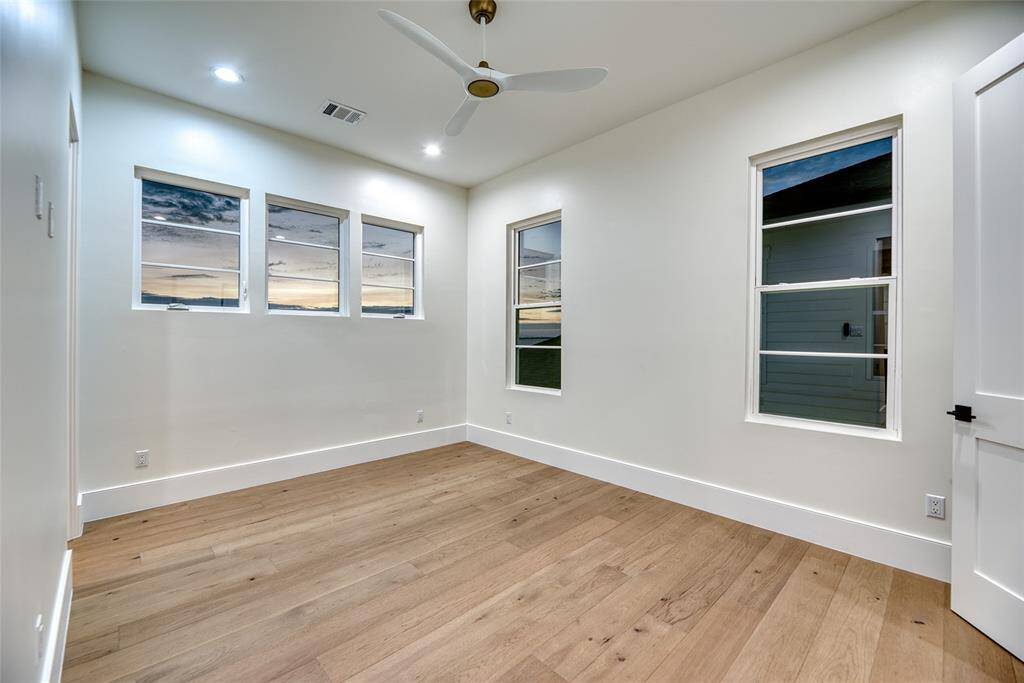 This bright, spacious second level bedroom features large windows, hardwood floors, and a ceiling fan, creating an inviting and airy atmosphere.