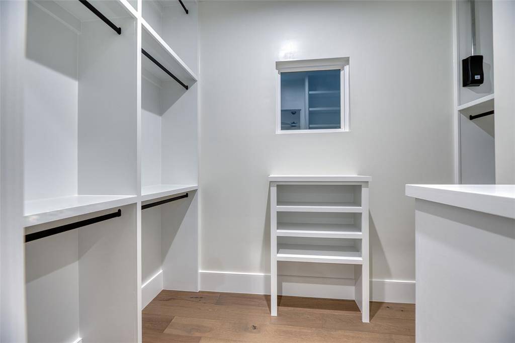 This photo showcases a spacious, modern walk-in closet with ample shelving and hanging space, featuring sleek white finishes and hardwood flooring, ideal for organized storage.