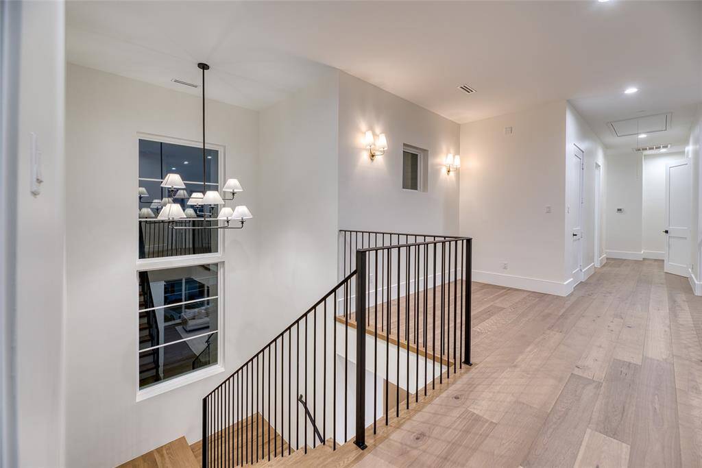 This photo shows a modern, well-lit hallway with light wood flooring and white walls. It features a staircase with a sleek black metal railing and a large window. Stylish light fixtures add to the contemporary feel.  Extra space would make great seating area.