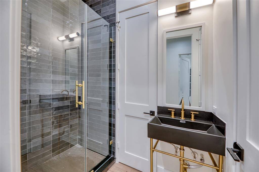 This modern second floor bathroom features a sleek glass-enclosed shower with stylish tile and gold fixtures. A chic black sink with matching gold accents complements the sophisticated design.