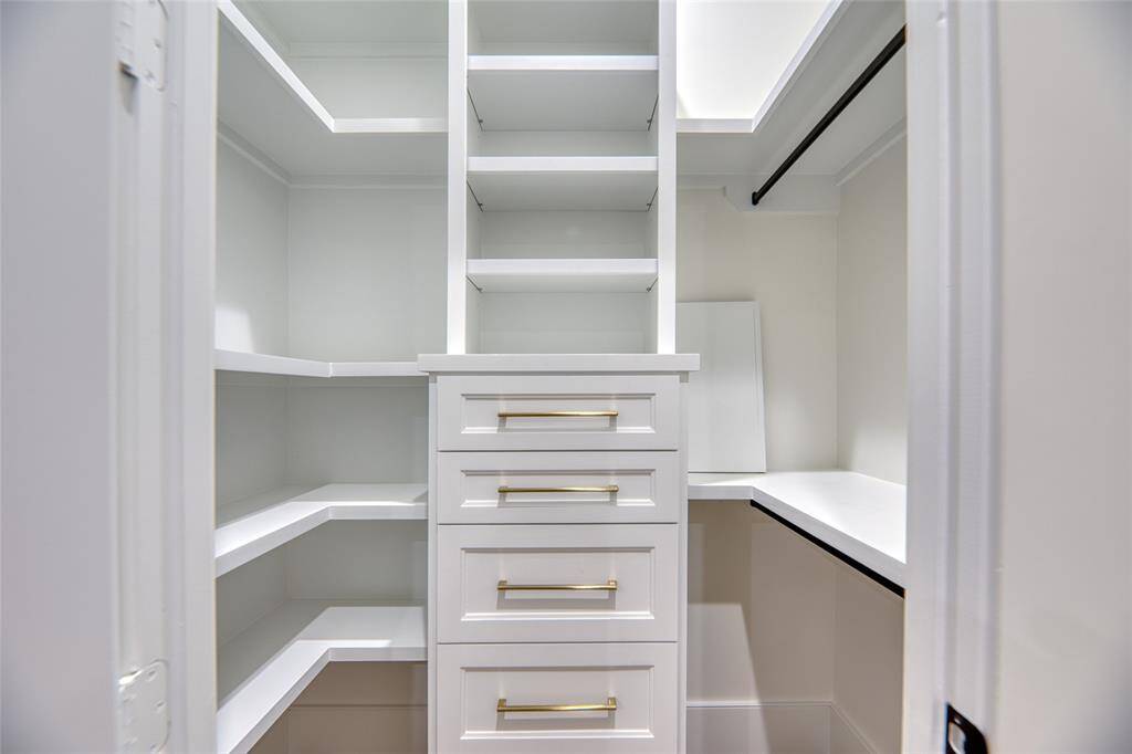This photo showcases a spacious, well-organized walk-in closet with ample shelving, drawers, and hanging space, featuring modern white cabinetry and sleek gold handles.