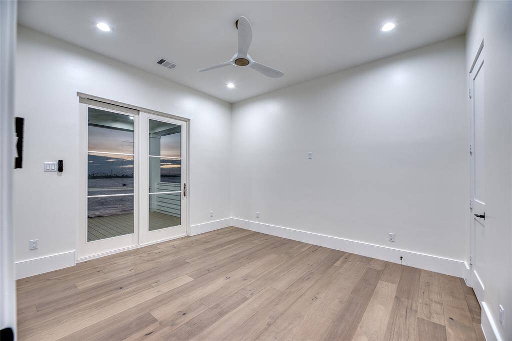 This second floor bedroom features a sleek, modern design with light wood flooring and recessed lighting. It includes a ceiling fan and large glass doors that open to a view of the water, providing ample natural light and a serene atmosphere.