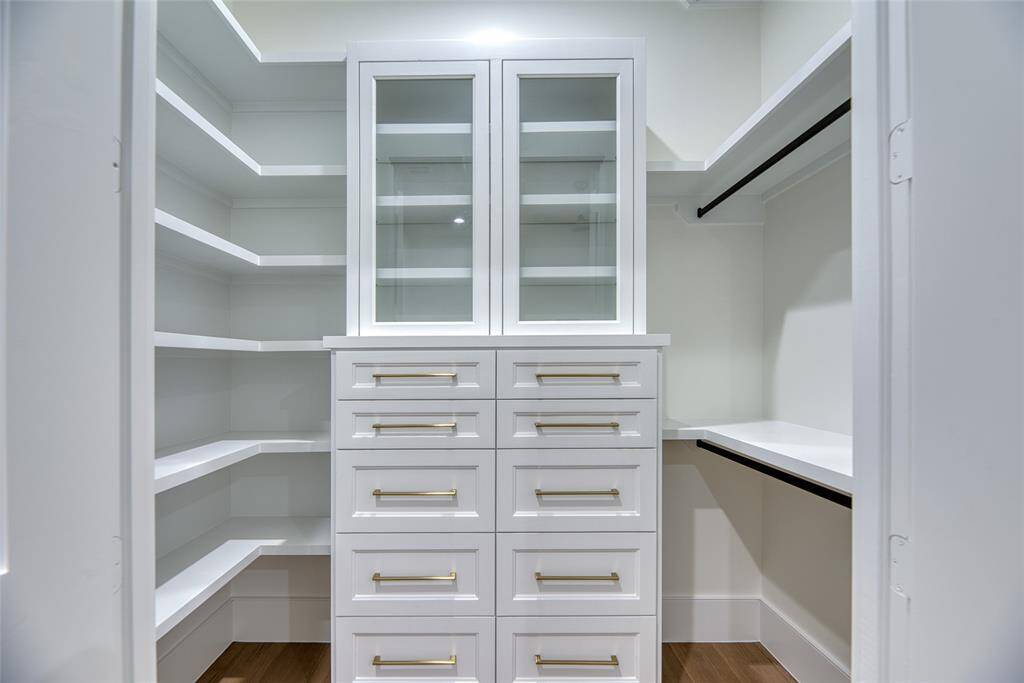 This is a spacious, well-organized walk-in closet featuring multiple shelves, a central drawer unit with glass-front cabinets, and hanging rods, all in a clean white finish.