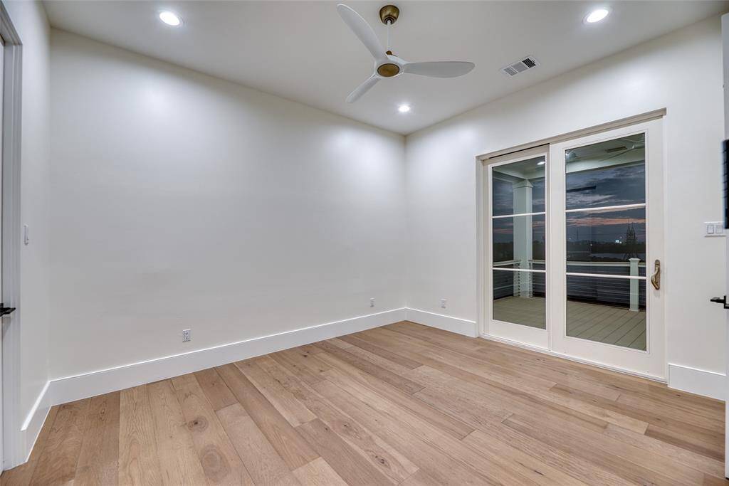 This room features light wood flooring, recessed lighting, and a ceiling fan. It has a clean, modern look with large sliding glass doors leading to a balcony, offering a view of the outdoors.