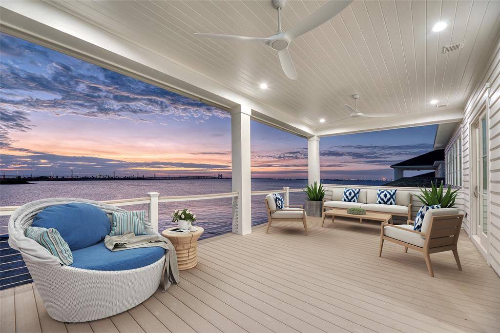 This photo showcases a spacious covered patio with comfortable seating, stylish decor, and ceiling fans. It offers breathtaking waterfront views and a serene sunset backdrop, ideal for relaxation and entertaining. Virtually staged.