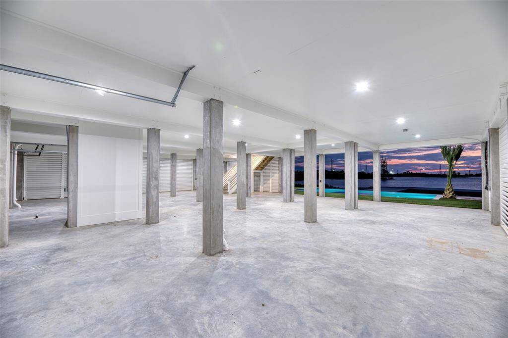 Spacious open garage  area with concrete flooring, multiple columns, and bright lighting. Large windows offer stunning waterfront views with a beautiful sunset backdrop, perfect for storage or a versatile workspace.  Able to fit at least 7 vehicles.