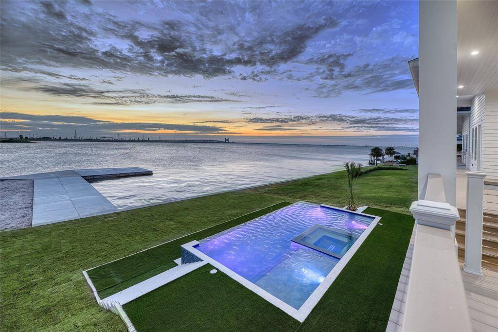 Stunning waterfront property with a modern infinity pool and spacious green lawn, offering breathtaking views of the sunset over the water. Perfect for luxurious living and outdoor entertaining.