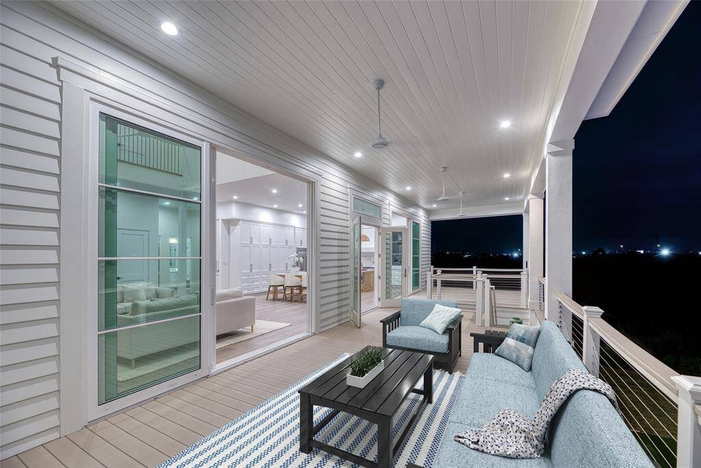 This photo showcases a spacious, well-lit outdoor deck featuring modern seating and a stylish ceiling with recessed lighting and fans. Large glass doors provide a seamless transition to the interior, revealing a bright and open living area. Ideal for relaxation and entertaining.  Virtually staged.