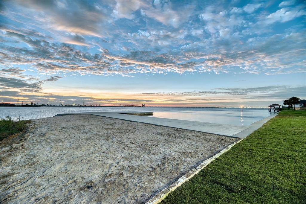 This photo showcases a serene waterfront setting with a sandy area, a lush green lawn, and a view of calm waters under a picturesque sky. Ideal for buyers seeking tranquility and scenic views.