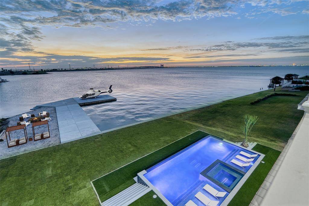 This stunning waterfront property features a luxurious infinity pool with sun loungers, a spacious grassy area, and a private dock with a helicopter pad that could be used to dock boat, fish off or and swim. Enjoy breathtaking sunset views over the expansive waterway, perfect for relaxation and entertainment.