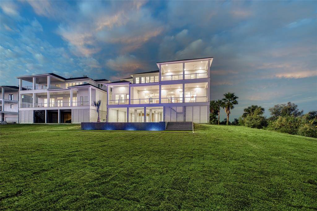 This modern, multi-story home features extensive glass and balcony spaces, offering panoramic views. It’s set on a spacious, manicured lawn with a contemporary aesthetic and vibrant lighting, perfect for enjoying scenic sunsets.