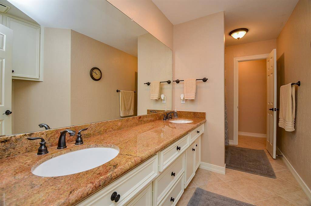 This secondary bathroom caters to all creature comforts,with vibrant counter tops hosting dual sinks, vanilla toned cabinetry below, and a shining wall-wide mirror above.
