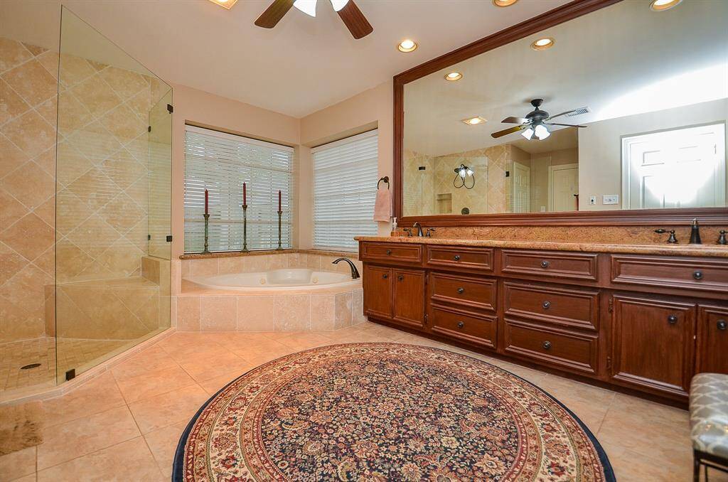 A super long counter top hosts dual sinks with lots of rich cabinet storage below, and a gorgeous wall-wide wood framed mirror, above. The spacious rimless, walk-in, glass enclosed shower is tempting, with luxurious soaking tub nestled beneath dual windows.
