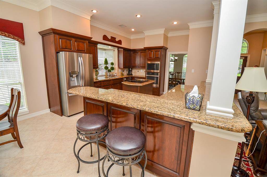 Gleaming dark cabinetry is complemented by sand colored granite counter tops and tumbled travertine backsplash in this truly workable kitchen, with ample room for stools under the extended counter.