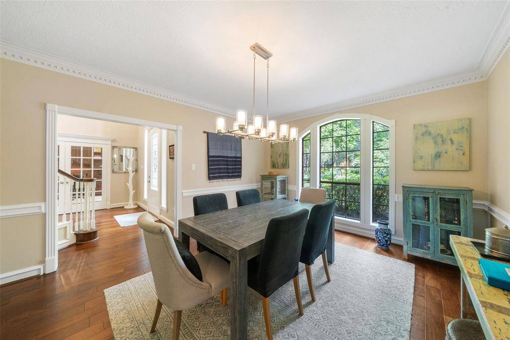 This dining room features elegant hardwood flooring, a large window with garden views, and a modern chandelier.