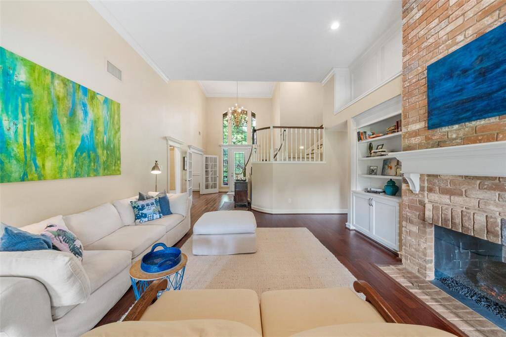 This spacious living room features high ceilings, dual brick fireplace, and hardwood floors. The room is bright and airy, with large windows and an open layout. A contemporary staircase add a modern touch, while built-in shelving offers additional storage.